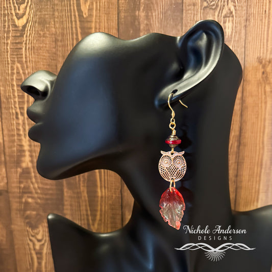 Brass Owl Earring with Red leaf glass pendant below displayed on a black mannequin ear with 'Nichole Anderson Designs' branding.