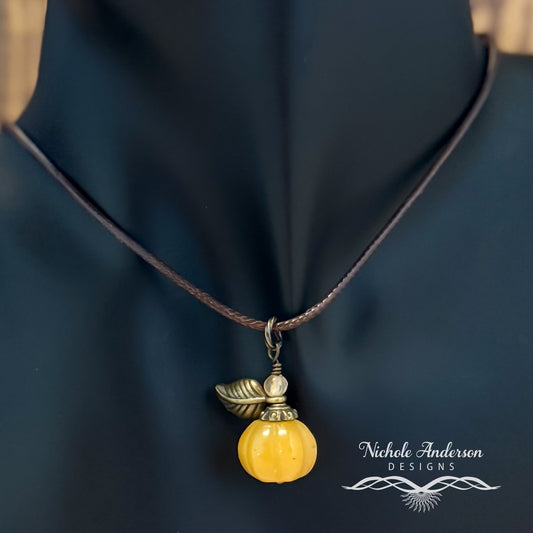 A carved Malaysian jade pumpkin, elegantly adorned with a bronze bead cap and leaf, topped with a faceted agate. Hangs on brown nylon cord and show on a mannequin's neck