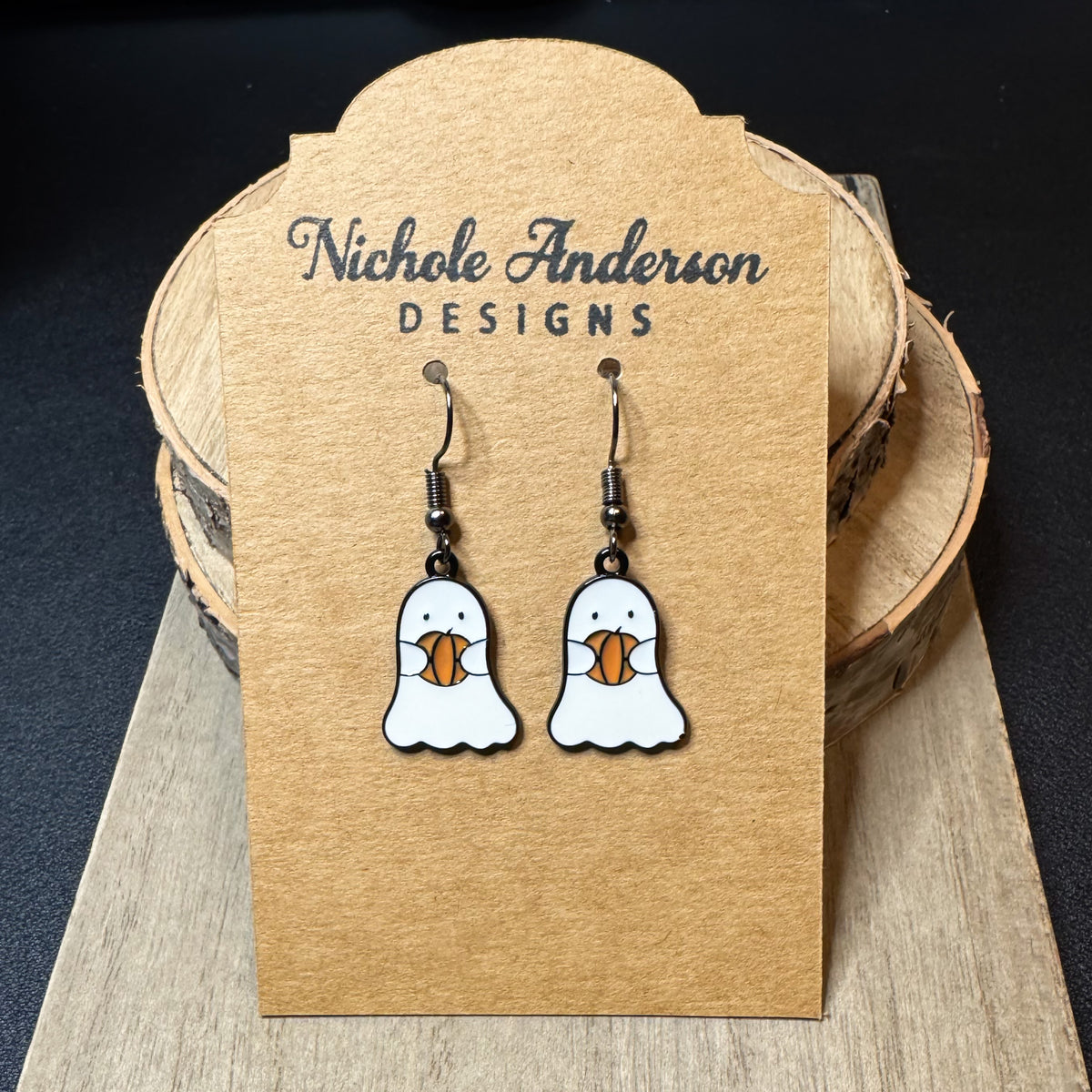 Pair of Enameled Ghosts holding a pumpkin hanging on a earring card designed by Nichole Anderson Designs