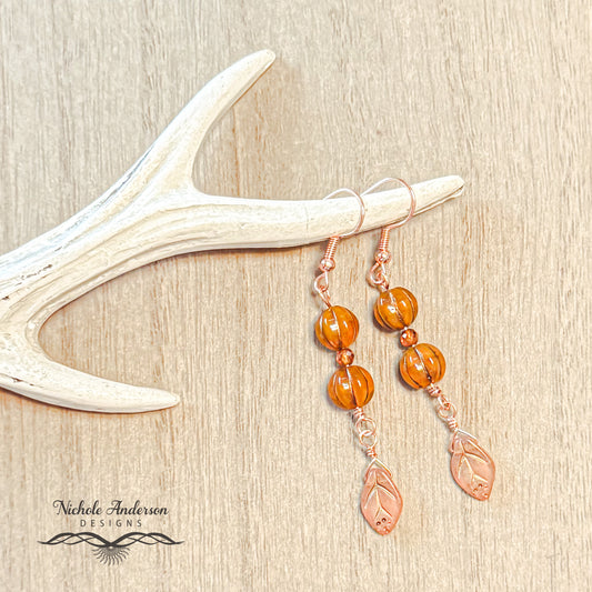 A pair of Pumpkin Hessonite Garnet Leaf Earrings displayed on wooden surface 